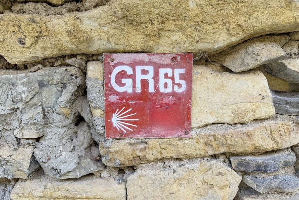 Plaque GR 65 rouge et blanche ornée d'une coquille, fixée sur un mur de pierres sèches