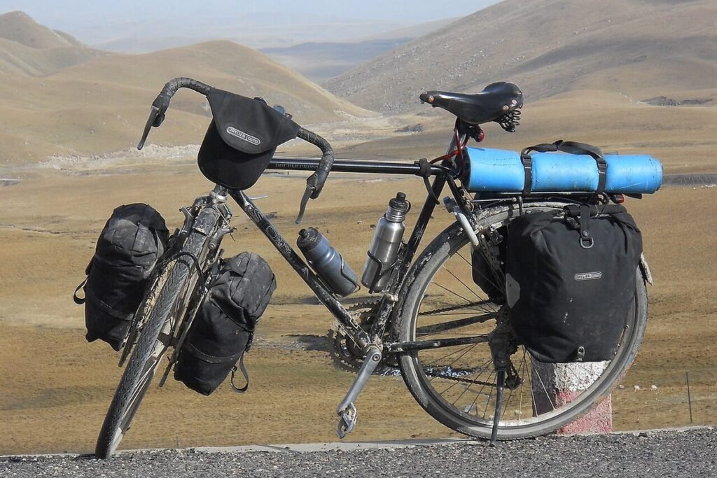 Vélo de randonnée chargé de sacoches et d'un tapis de sol, arrêté au bord d'une route de montagne