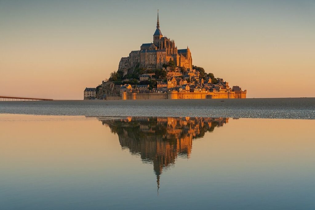 Le Mont-Saint-Michel au lever du soleil, son abbaye se reflétant dans l'eau de la baie